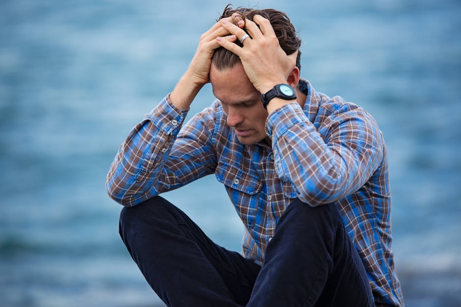 pexels-photo-897817-897817-3 A man in a plaid shirt sits by the water looking distressed, symbolizing stress.