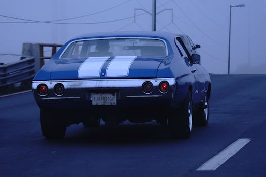 A classic blue coupe car driving on a misty road, showcasing speed and style in a foggy atmosphere.
