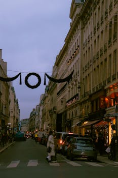 A bustling street scene in Paris at dusk, showcasing historic architecture and city life.