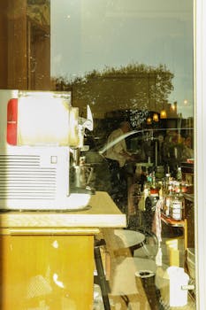 View through a window into a bustling cafe in Paris, capturing daily hustle with coffee machines and patrons.