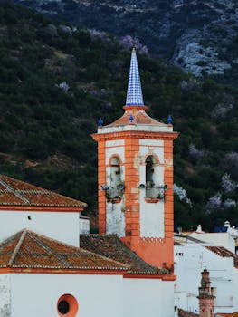 Picturesque church tower set against a mountainous backdrop in Cortes de la Frontera, Spain.
