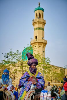 pexels-photo-30799112-30799112 Vibrant traditional horse riders in colorful attire near a mosque tower in Nigeria.