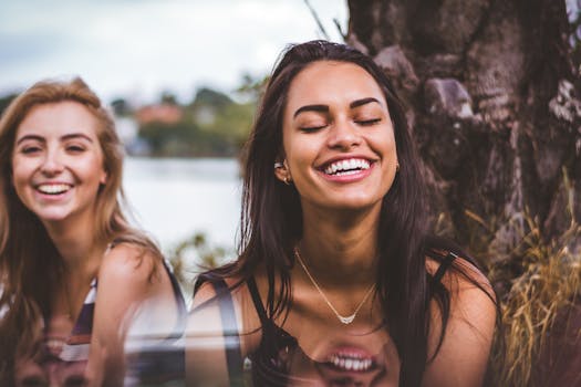 pexels-photo-908602-908602 Two women happily laughing together outdoors by a serene lakeside.