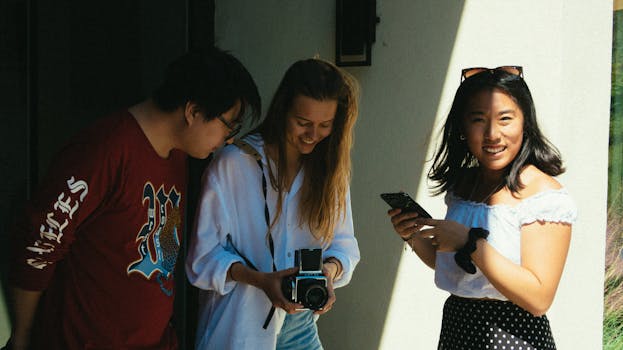Three young friends smiling, sharing moments with a camera and phone outdoors, enjoying a sunny day.