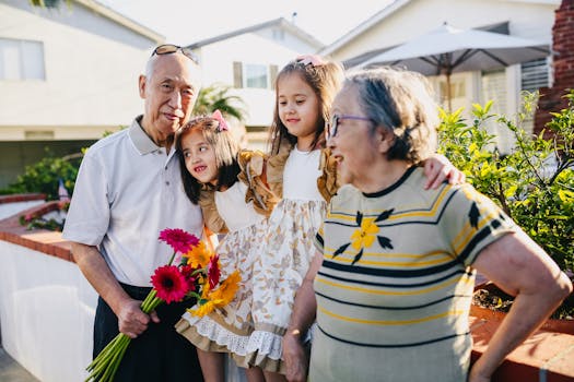 Asian grandparents with twin grandchildren enjoying a sunny day outdoors with flowers.