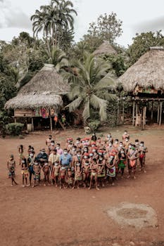 Aerial view of indigenous people in traditional attire gathered in a rural village setting.