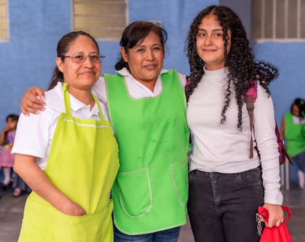 Three women indoors, smiling and wearing green aprons, showing togetherness.