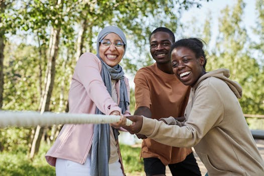 Friends of diverse backgrounds enjoy a tug of war game outdoors in a natural setting.
