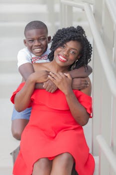 A cheerful African American mother and son share a loving hug on a staircase, both smiling brightly.